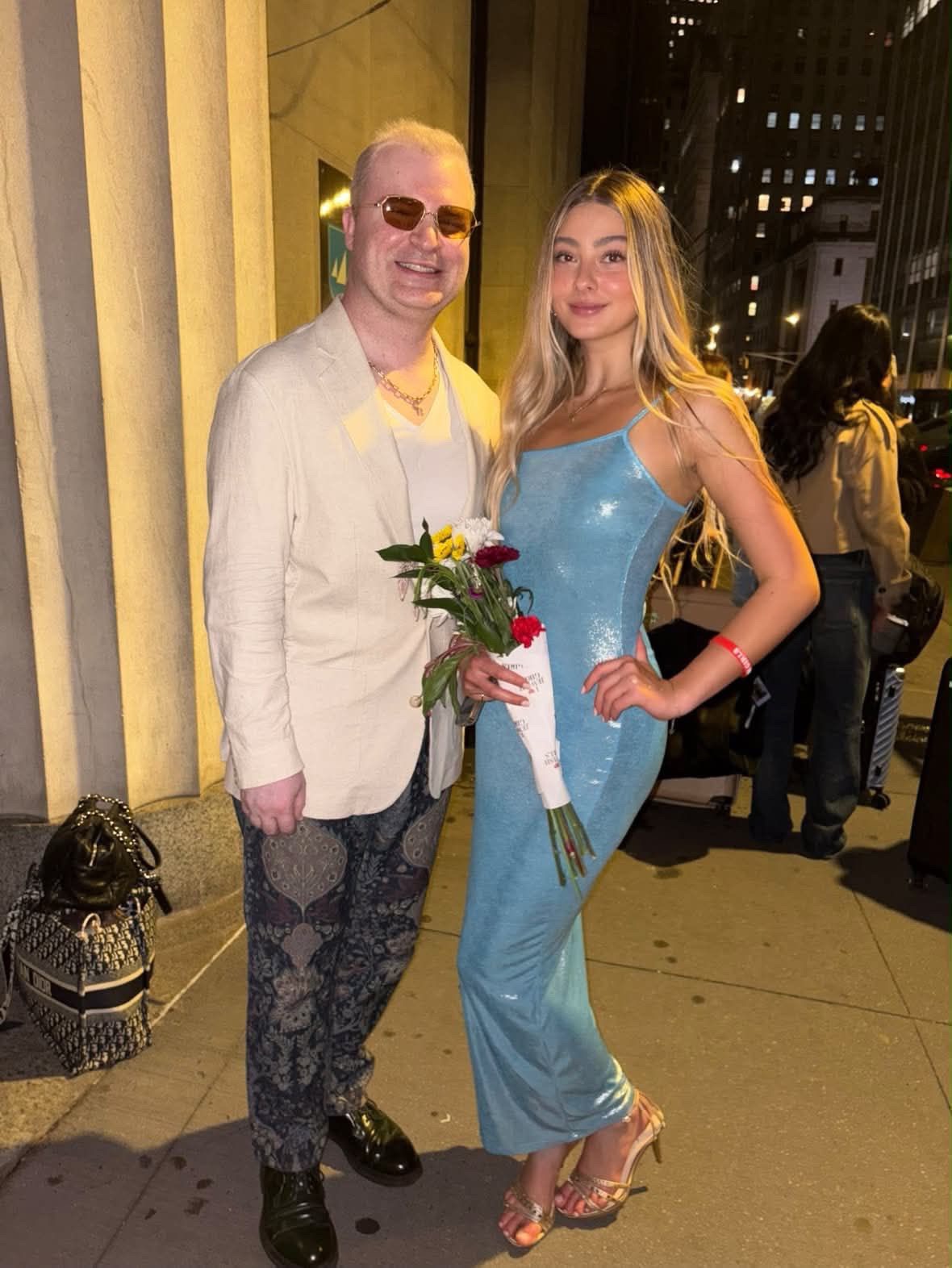 Two people posing together at a formal event venue with city views visible in the background.