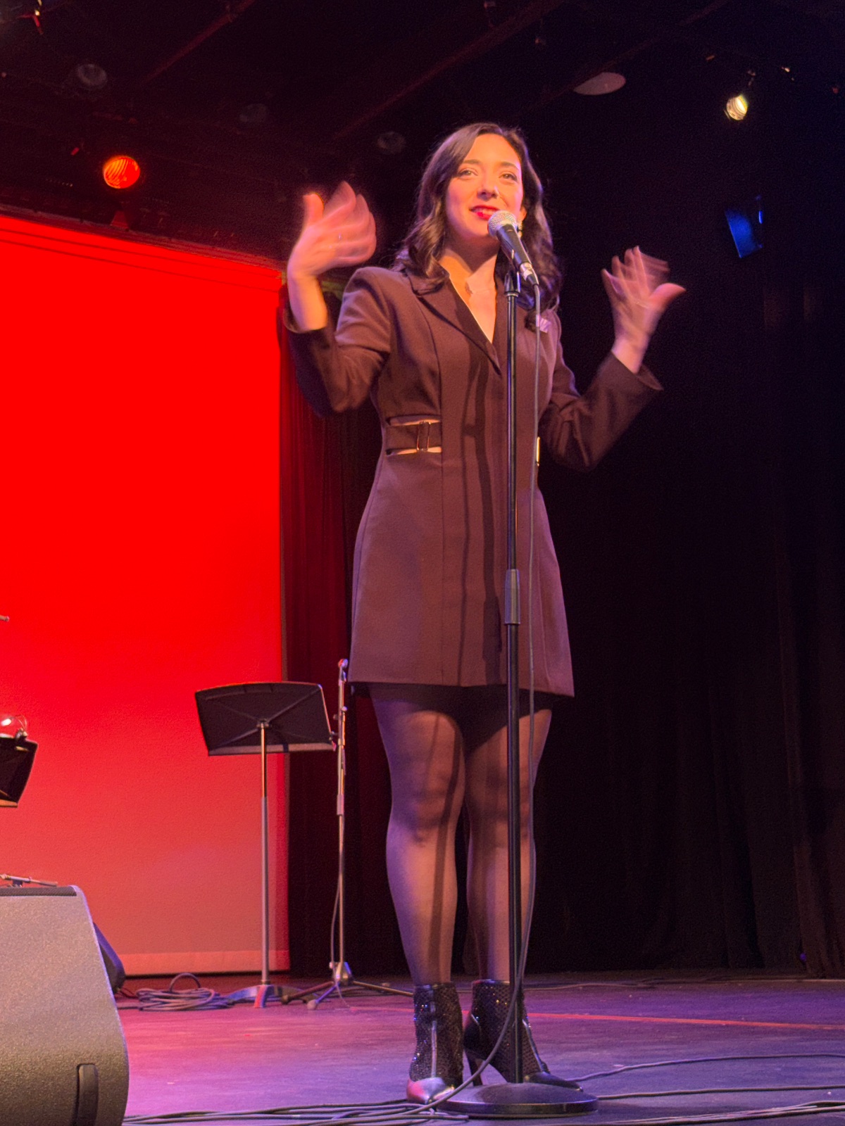 A performer on stage with dynamic lighting, making expressive gestures during a vocal performance.