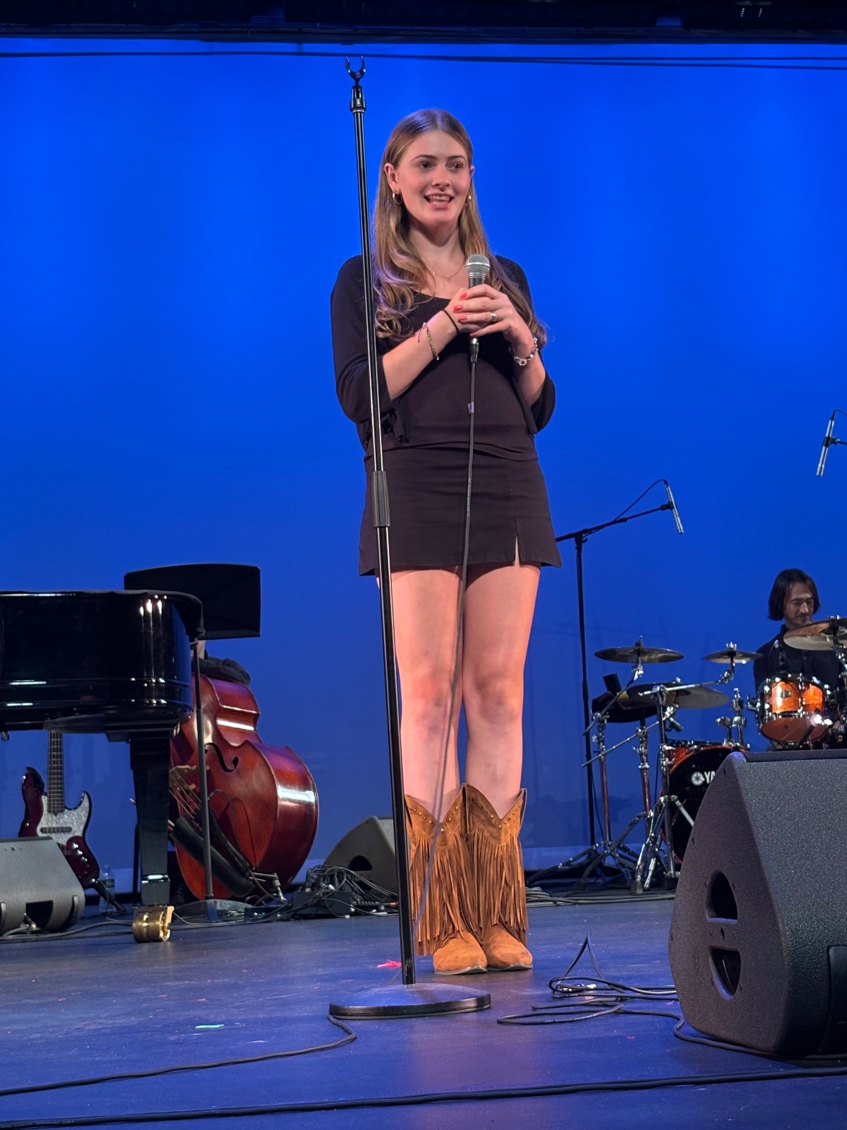 A performer stands on stage under bright lighting, engaging with a live audience in front of them.