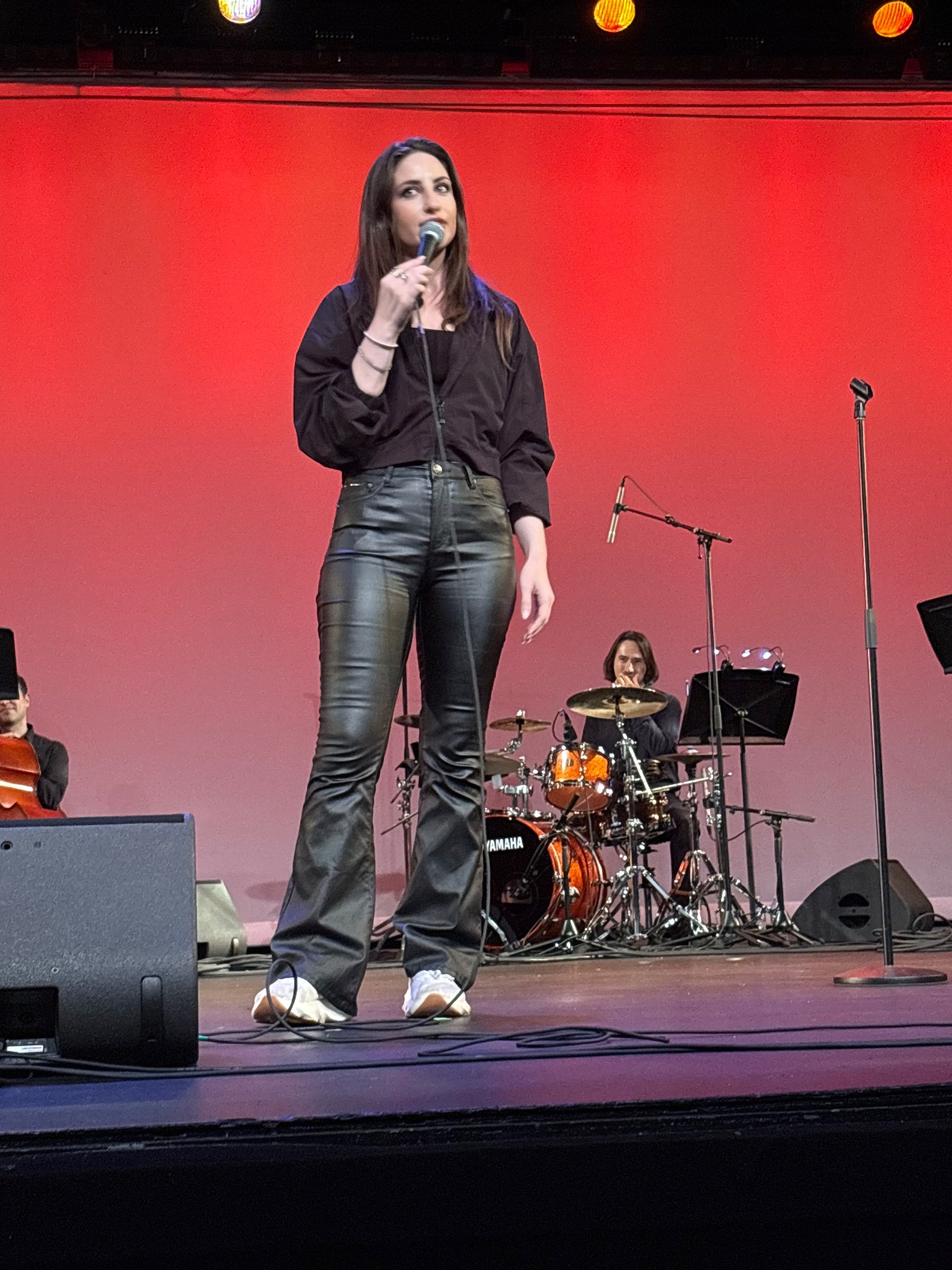 A performer on stage with a band under colorful stage lighting in an intimate venue.