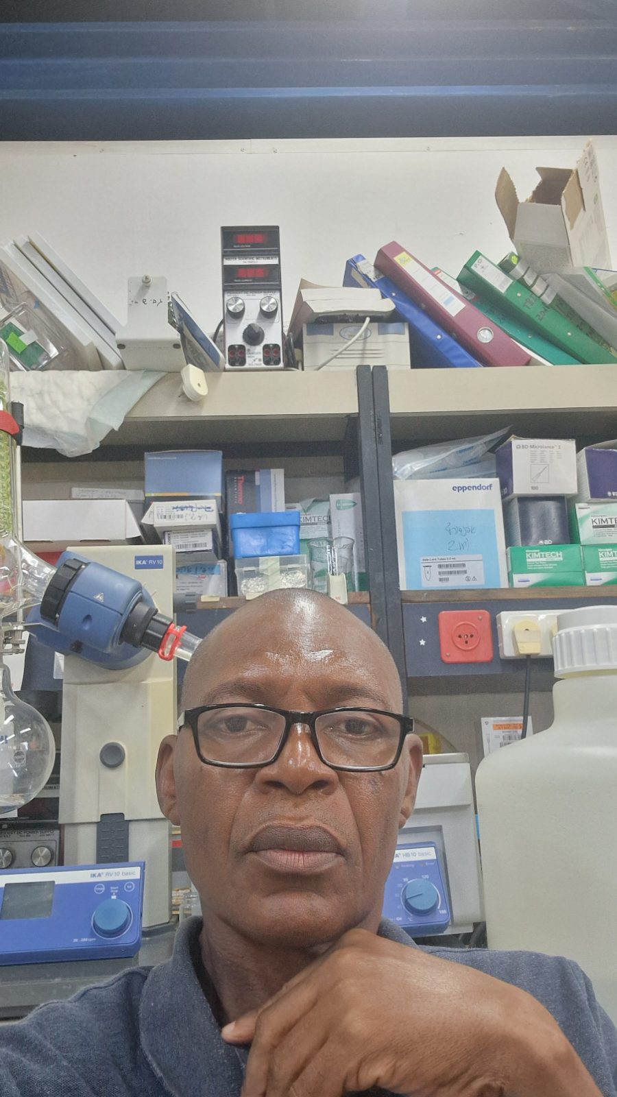 A person in a thoughtful pose with shelves of organized supplies and creative tools visible behind them.