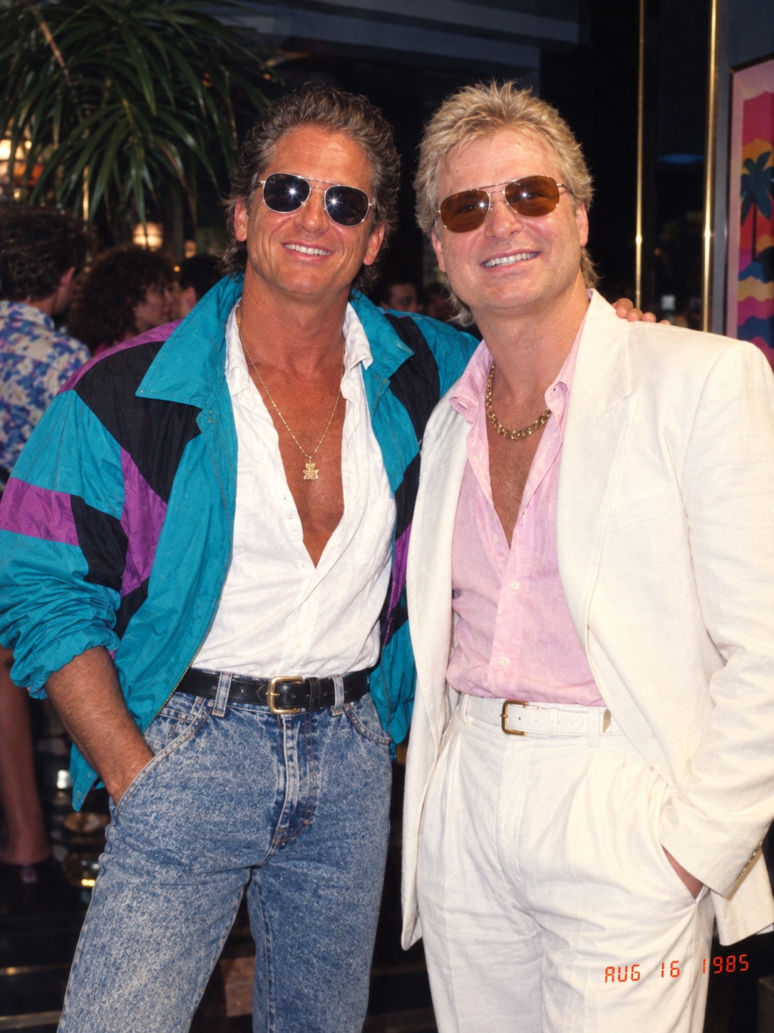Two people in bold 80s inspired fashion at an evening event, smiling together.