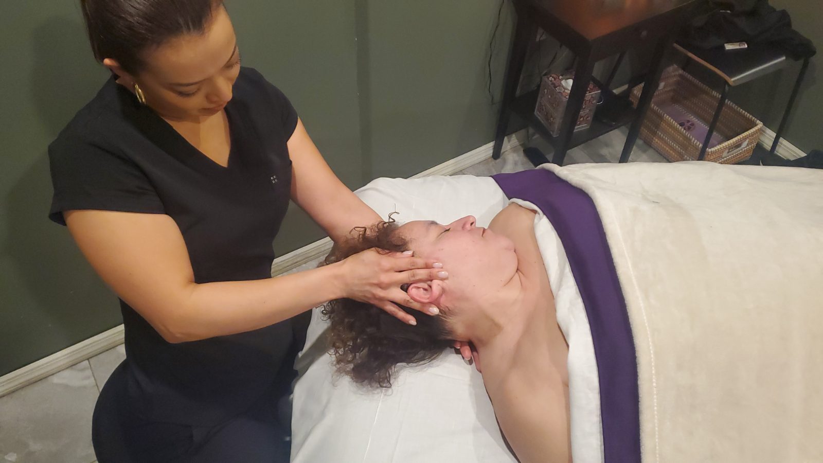 A practitioner applies facial massage techniques to a client resting on a treatment table.